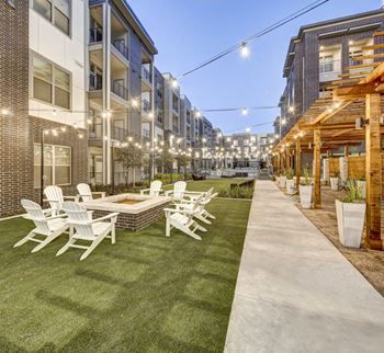 A patio with white chairs and a table is surrounded by apartment buildings at Arise Riverside Apartments, Texas